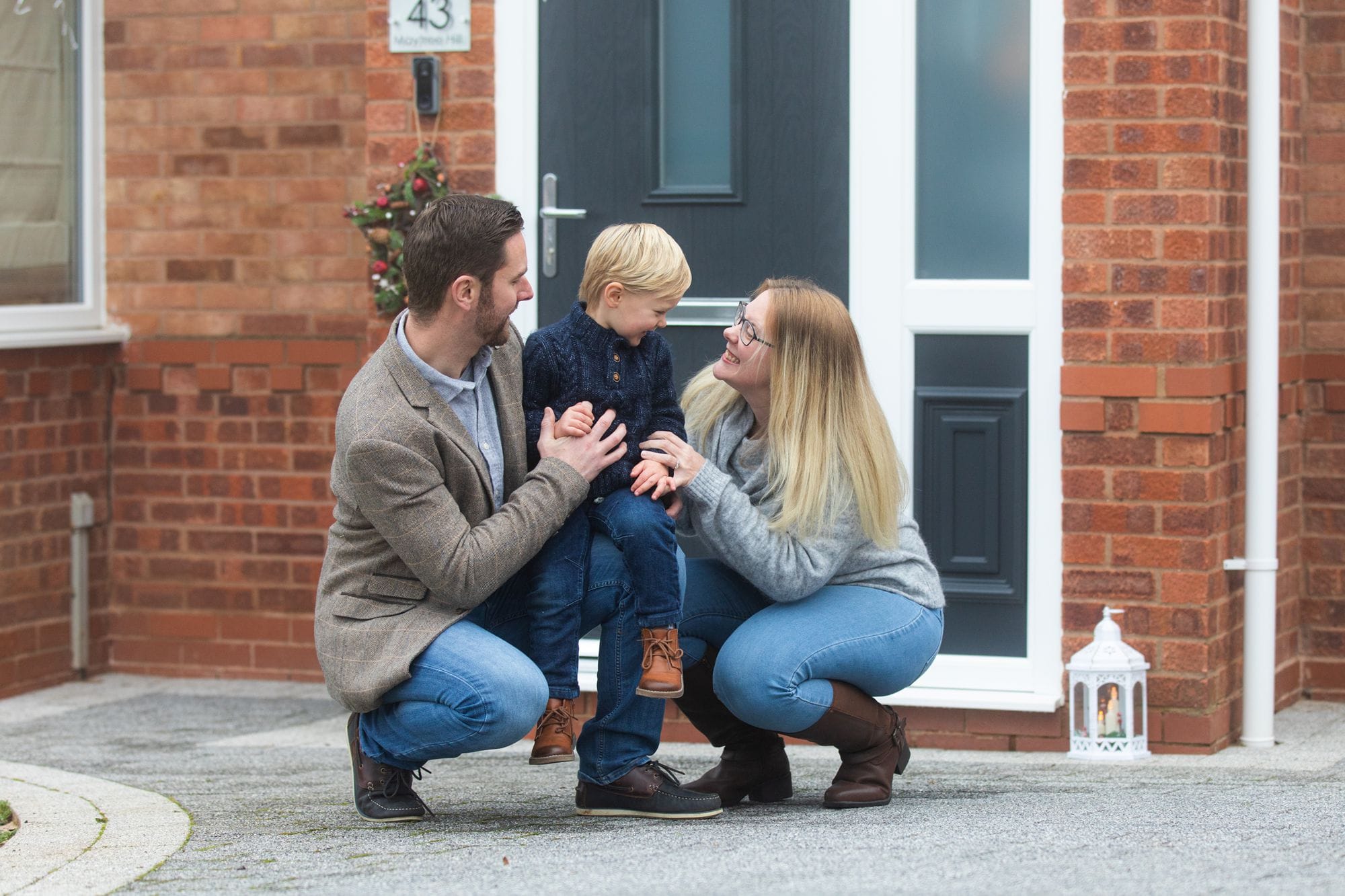 young family crouched on home driveway for photo session
