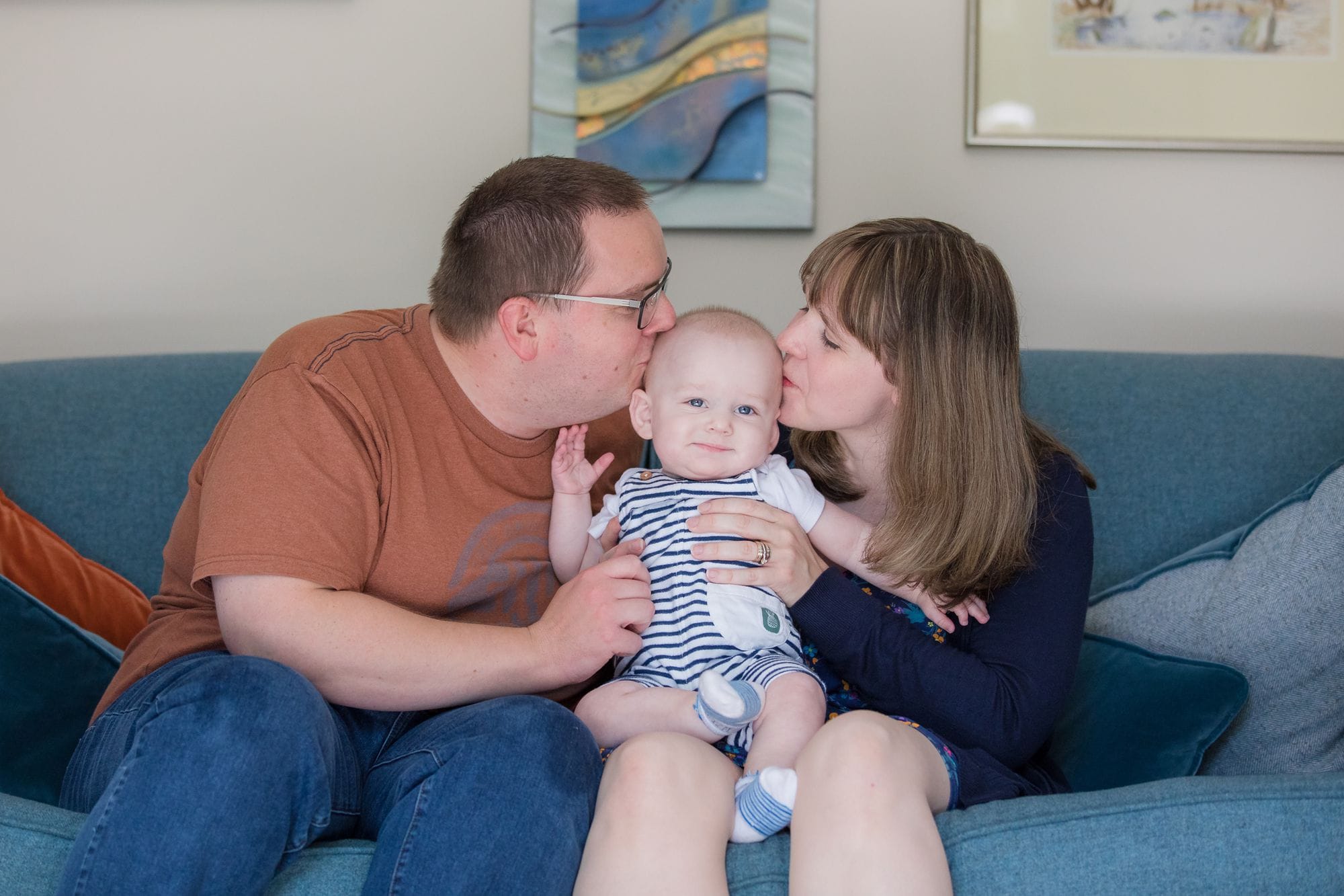 couple kissing their baby sat on sofa  at home during a family photo session