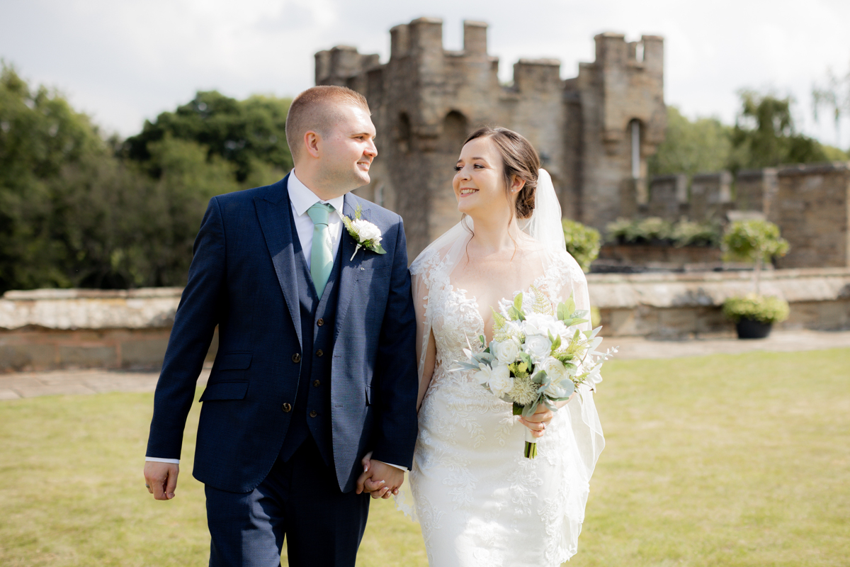 couple walking throguh grounds with castle turret in background at Arley house and gardens