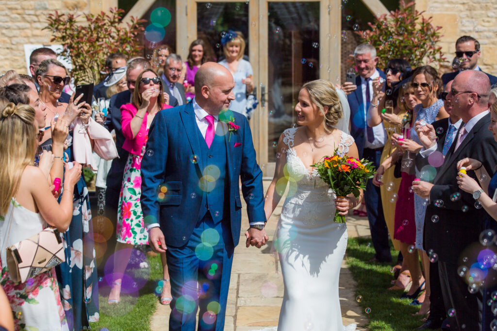 bride and groom walk towards the camera as guests blow bubbles at them on their wedding day at the abrn at upcote