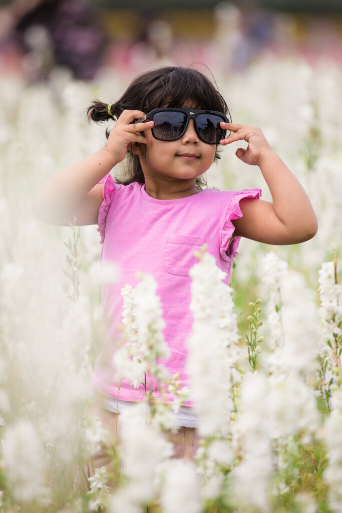 little girl wearing sunglasses standing in white flower field at pershore