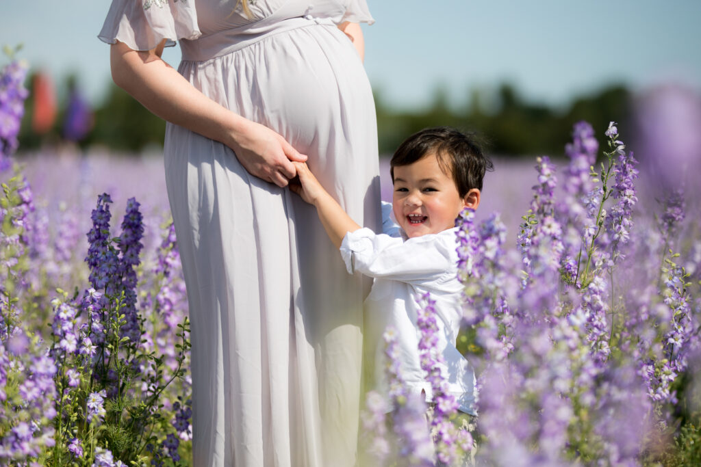little boy hugging pregnant mother's belly in colourful flowers at pershore confetti fields