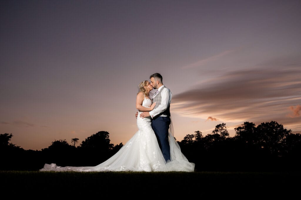 bride and groom kissing standing against purple sunset sky