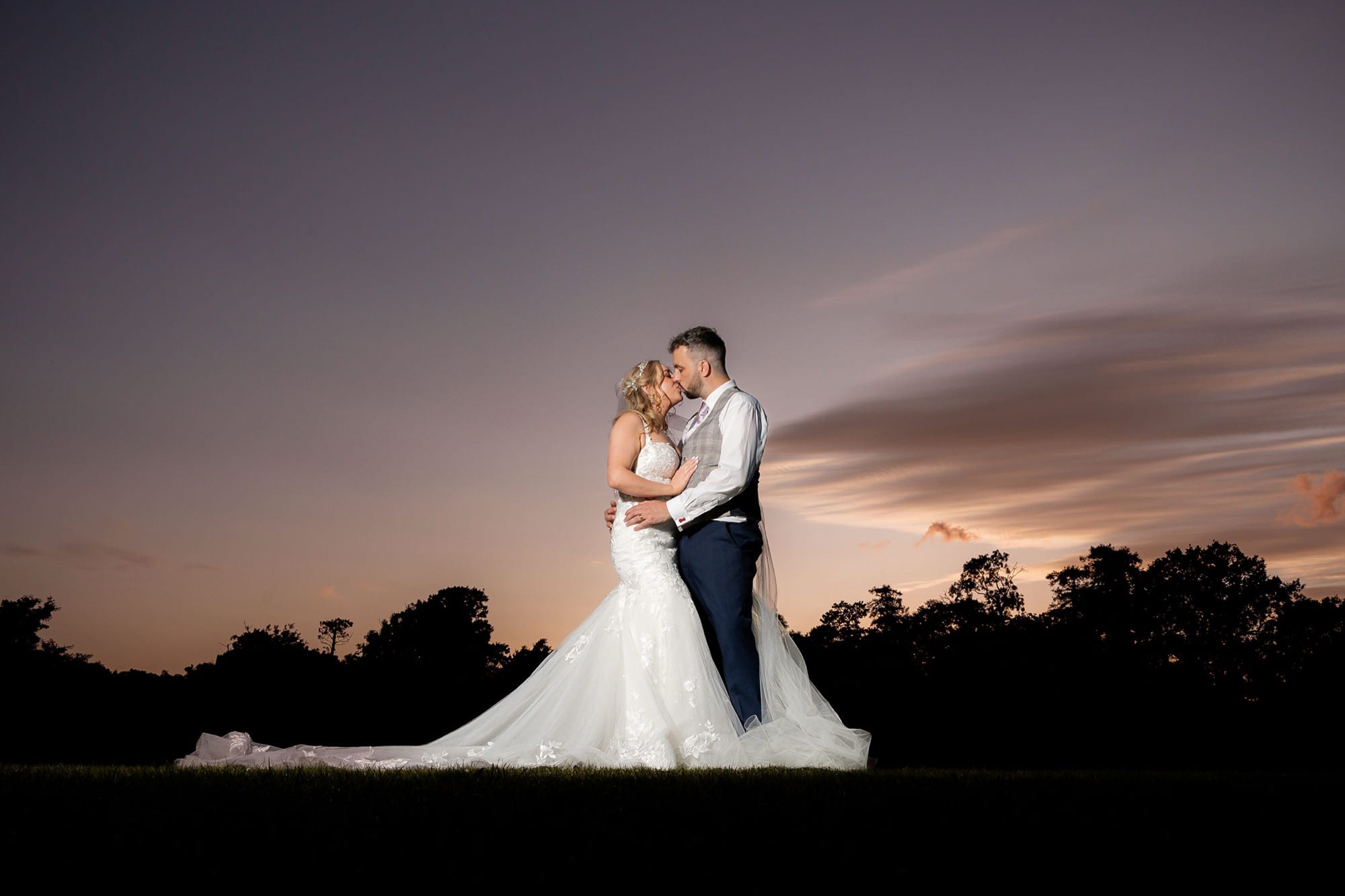 bride and groom kissing standing against purple sunset sky