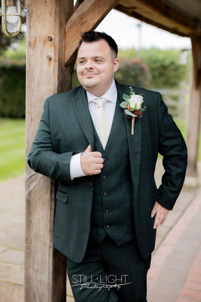 groom stood against wooden post getting ready for wedding at redhouse barn