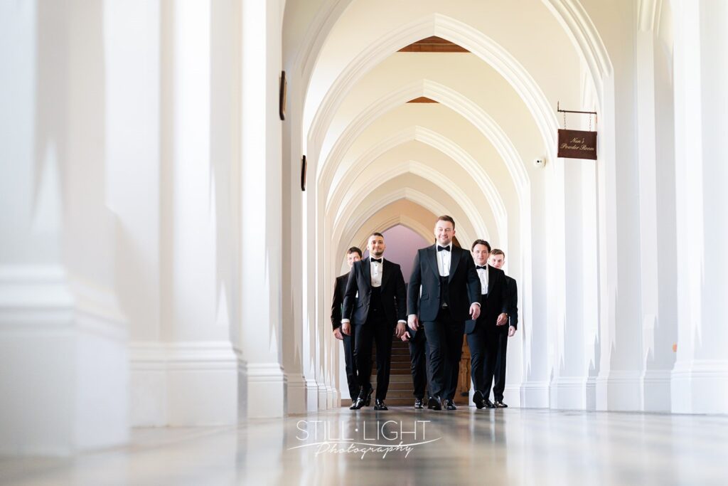 groom and groomsmen walking towards camera through cloisters corridor at stanbrook abbey
