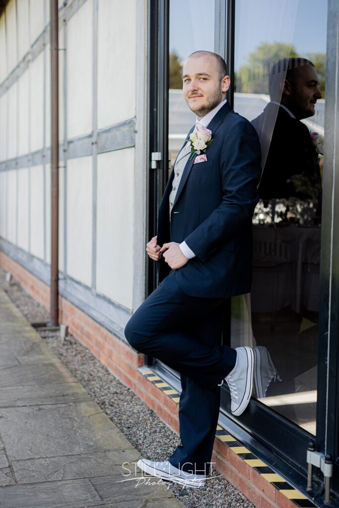 groom outside at redhouse barn wearing navy blue suit and grey trainers