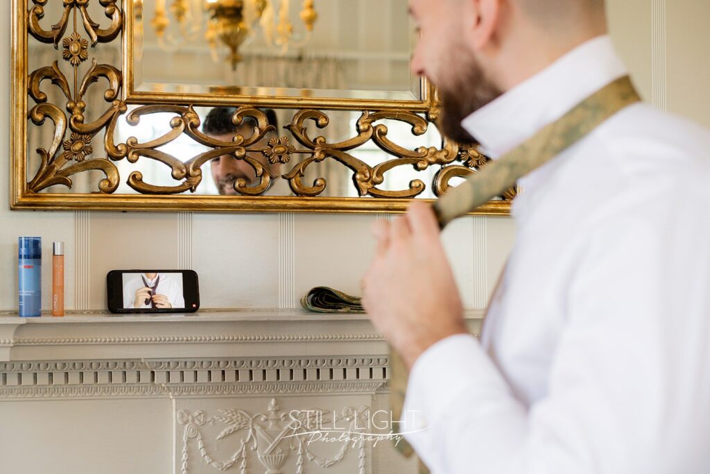 groom trying to tie his tie watching video tutorial on phone