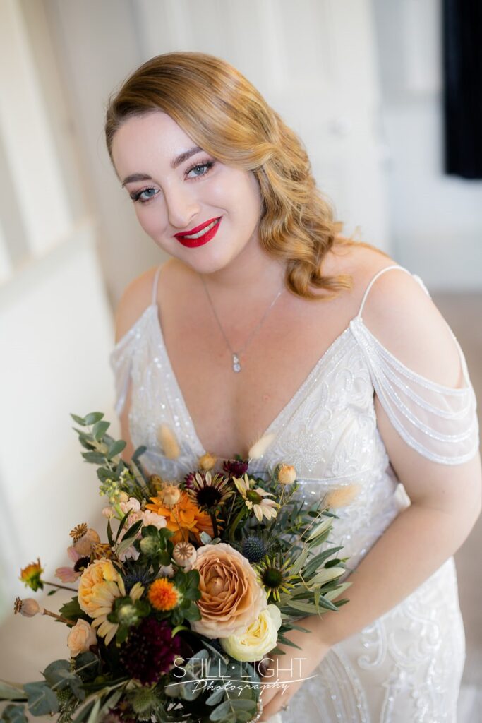 bride ready for her wedding day holding flowers and wearing vintage dress and red lipstick
