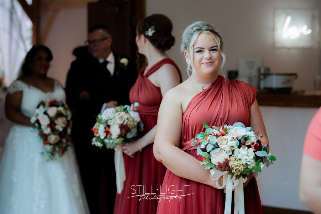 bridesmaid smiling at camera getting ready to walk into red brick barn for wedding ceremony