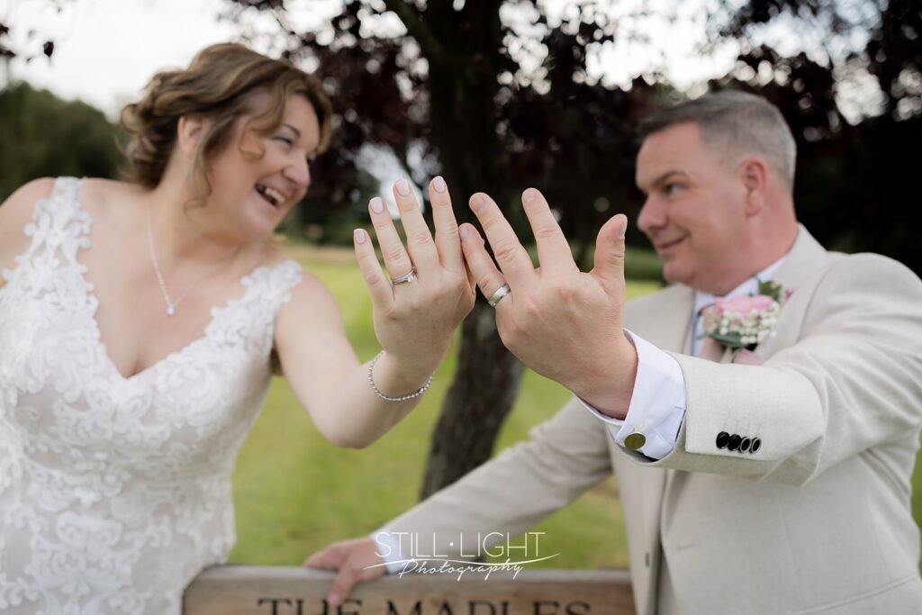 bride and groom show off their wedding rings to the camera