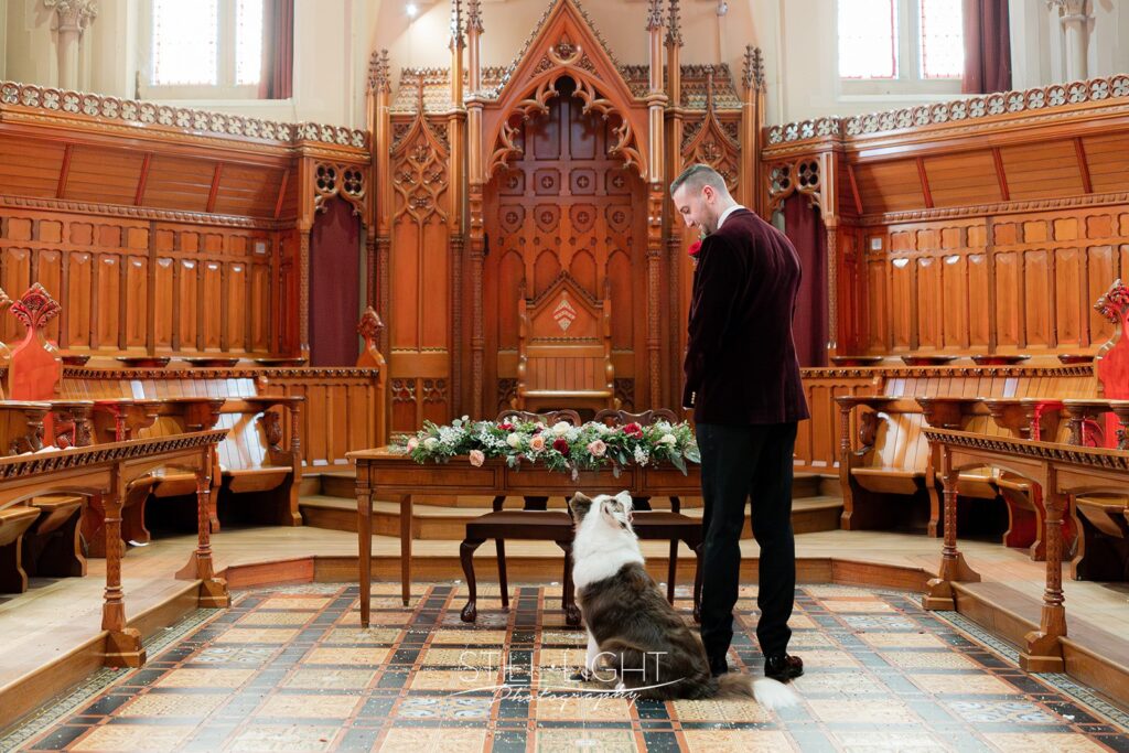 a groom standing at the altar in callow great hall at stanbrook abbey with his dog