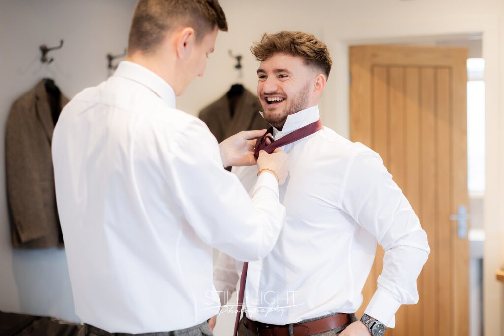 groom laughing while getting his tie fixed at bredenbury court barns
