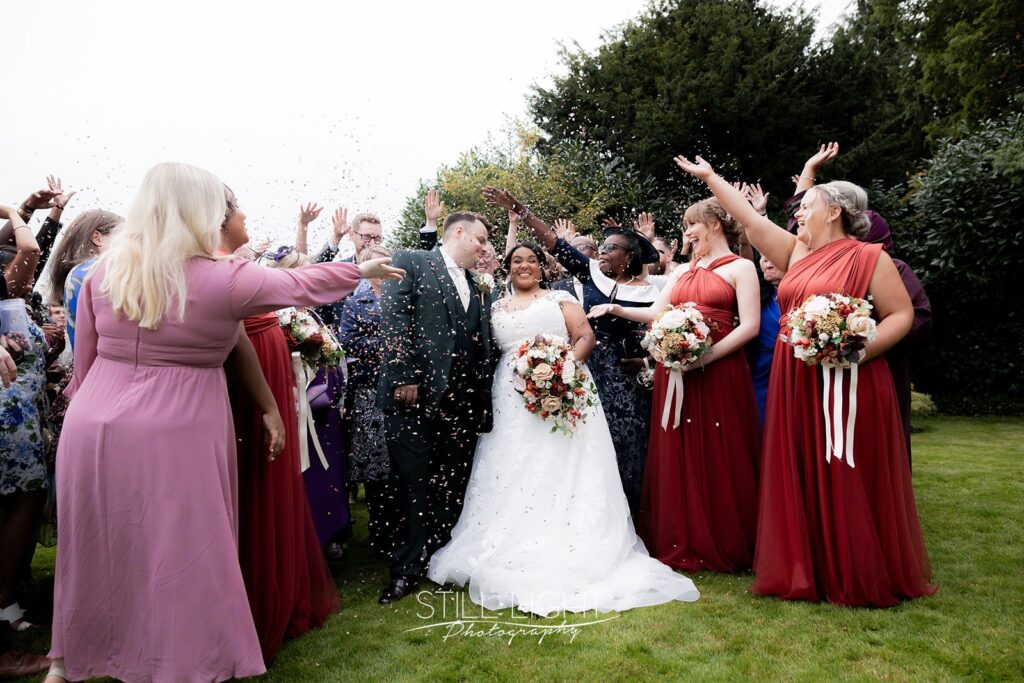 bride and groom surrounded by their guests who are throwing confetti