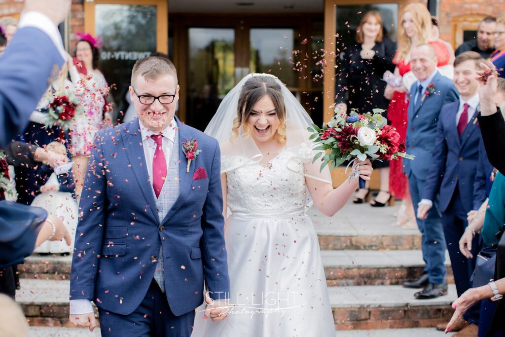 bride and groom walking towards camera laughing as confetti is thrown at wootton park