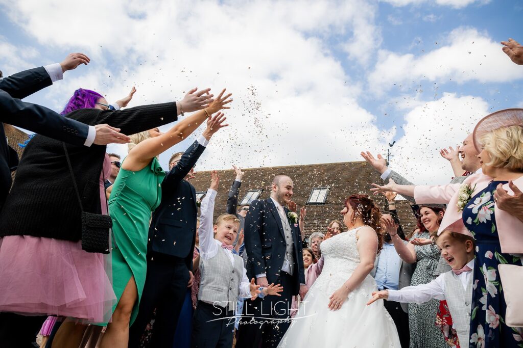 wide shot of sonfetti being thrown by guests onto bride and groom outside redhouse barn on spring wedding day