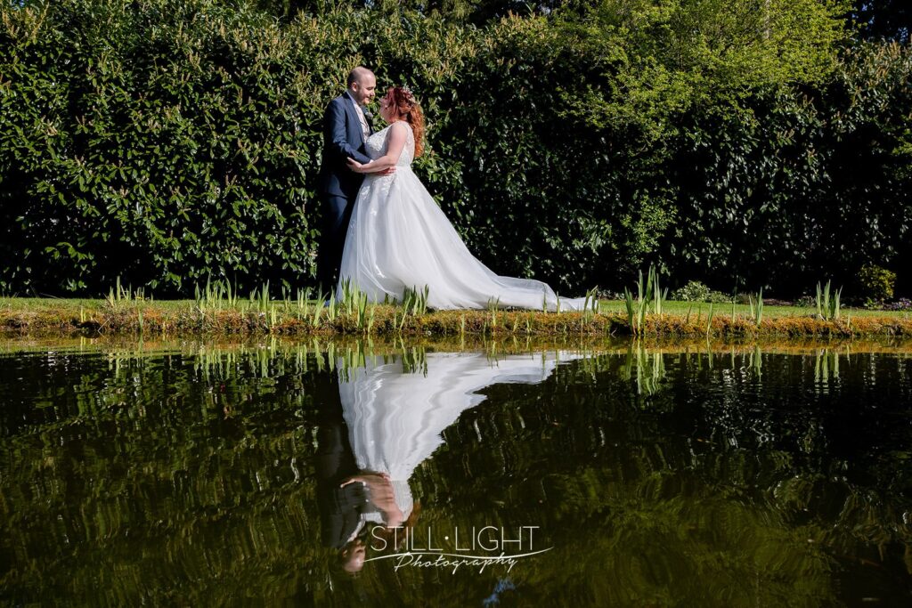 bride and groom standing in gardens at redhouse barn with reflection in pond water