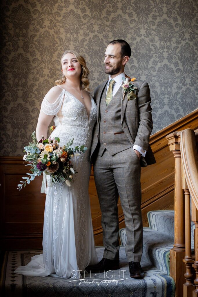bride and groom standing on staircase by window at brockencote hall