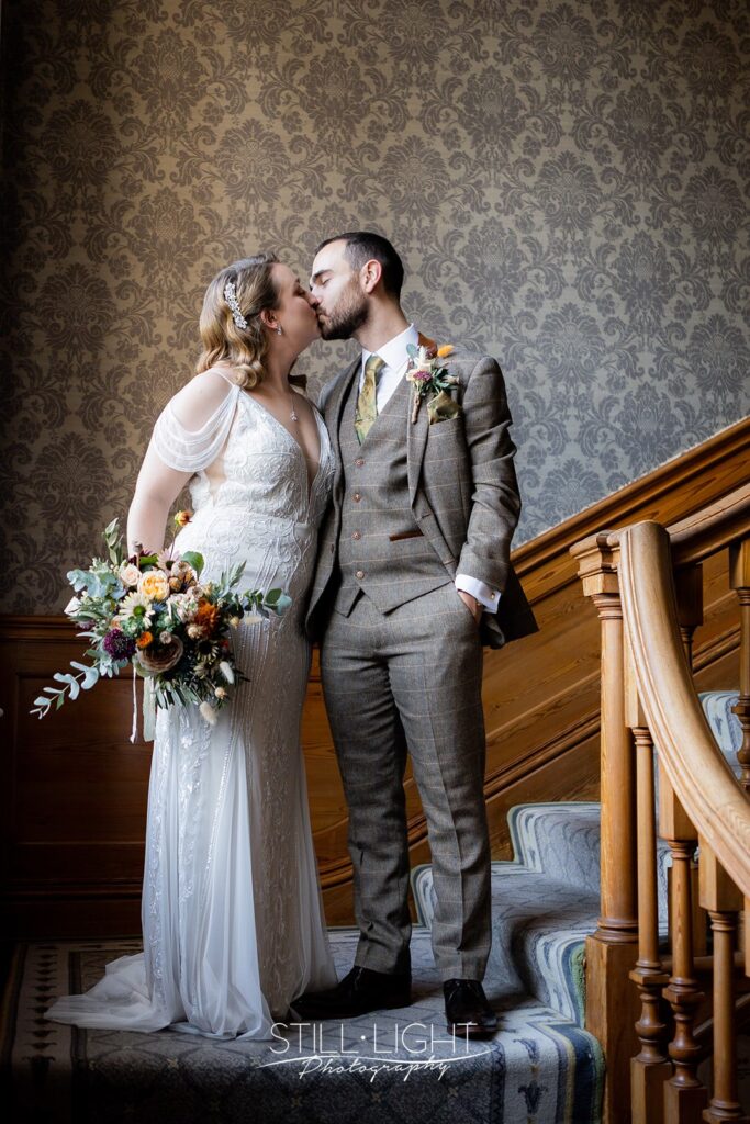 bride and groom standing on staircase by window at brockencote hall