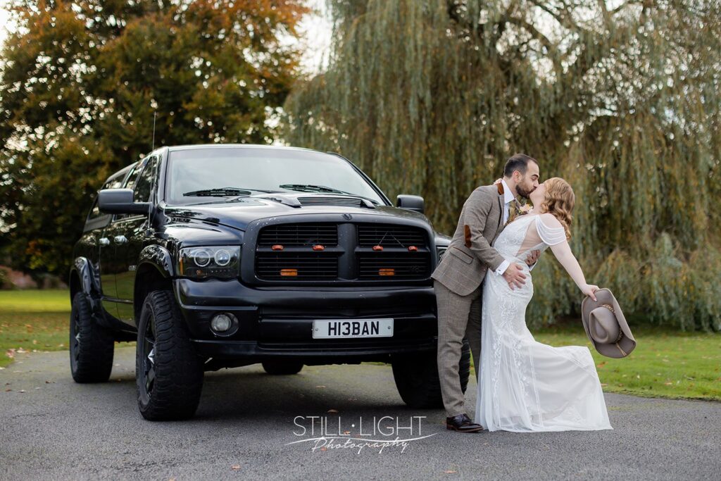 bride and groom kissing in front of hummer truck on their vintage wedding day at brockencot hall