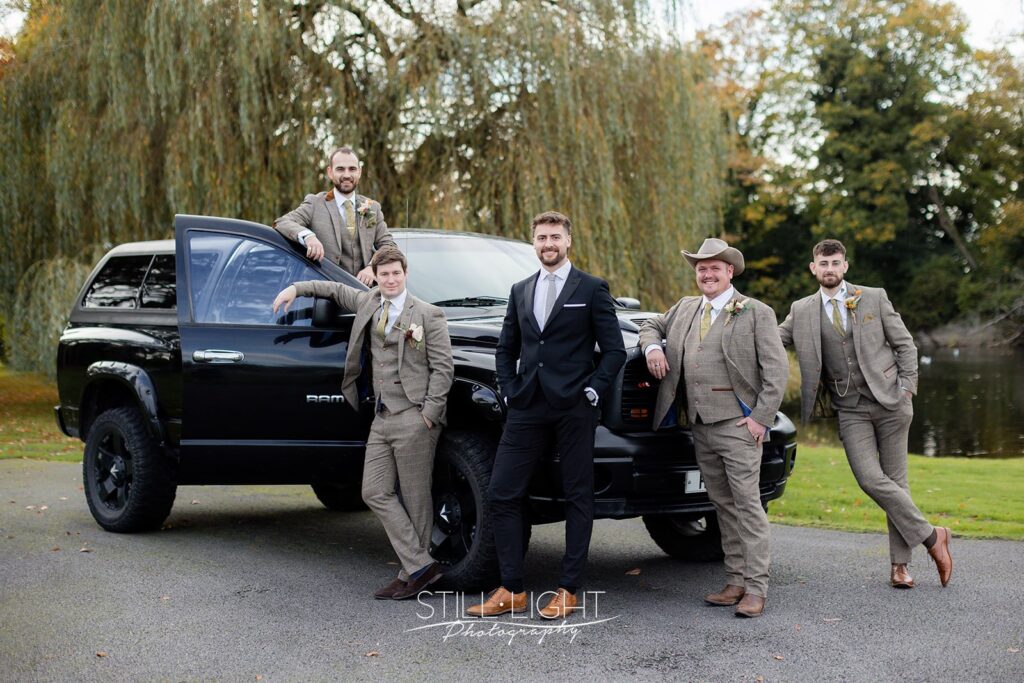 groomsmen standing around hummer truck wearing tweed on wedding day at brockencote hall