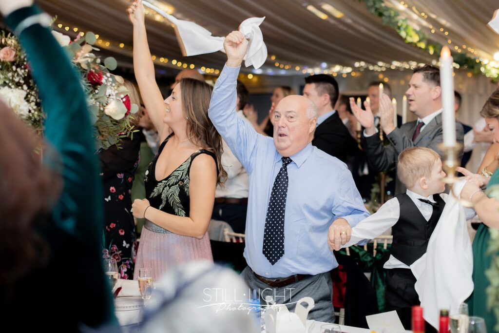 wedding guests cheering and swirling napkins as bride and groom enter their wedding breakfast at stanbrook abbey hotel