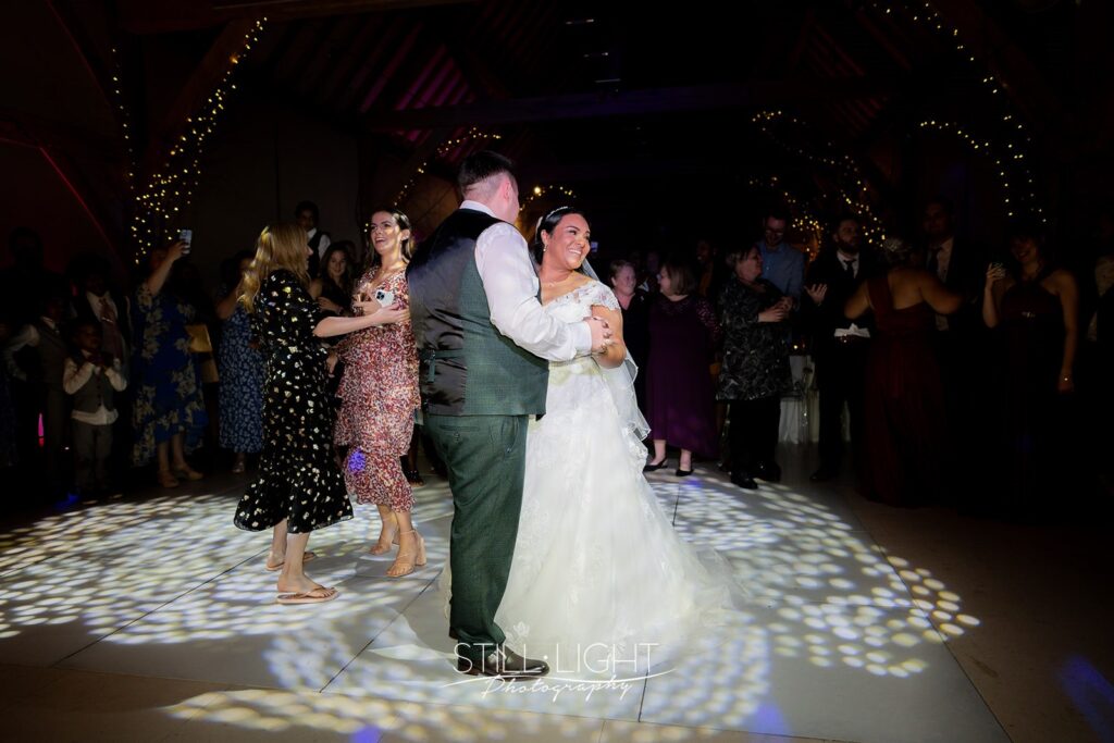 bride and groom on dancefloor with dark baclground surrounded by their guests also dancing