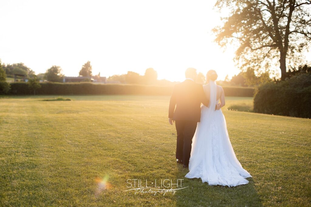 bride and groom at sunset walking away from camera on their summer wedding day at stanbrook abbey