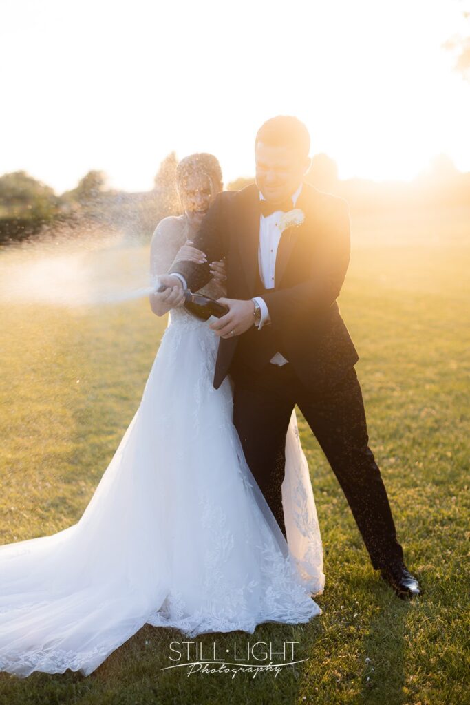 bride and groom at sunset spraying champagne from bottle