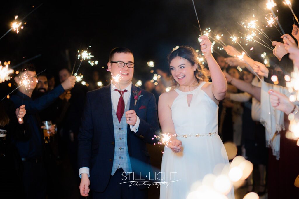 bride and groom surrounded by guests with sparklers held high