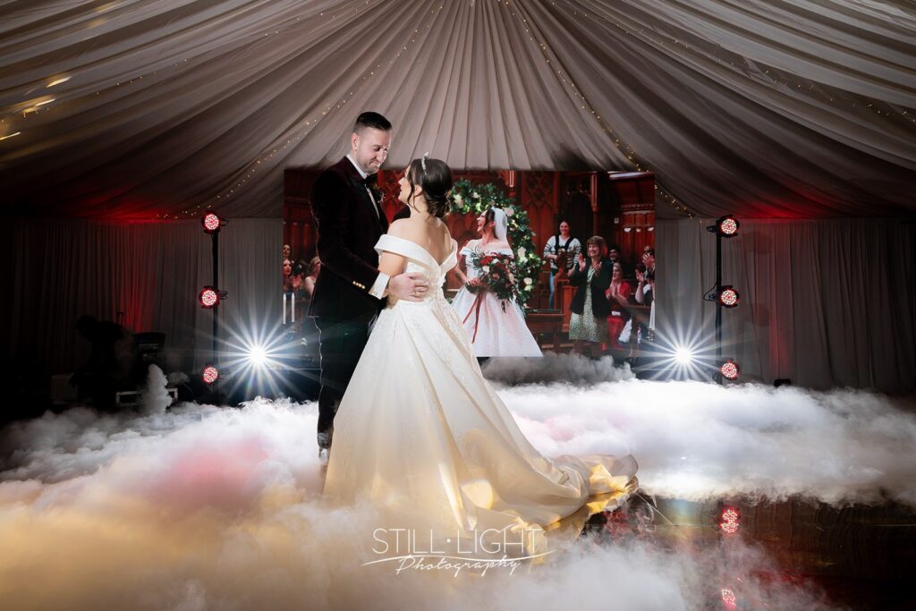 bride and groom dancing with dry ice on floor around them with lights in the background at stabrook abbey hotel