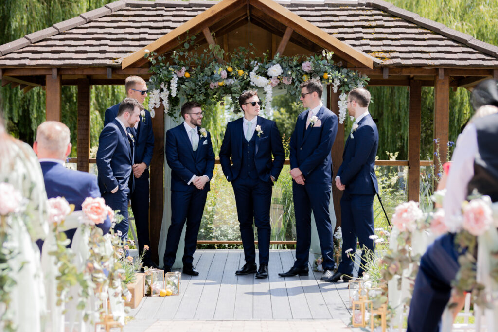 groomsmen waiting at front of aisle before lakeside wedding ceremony