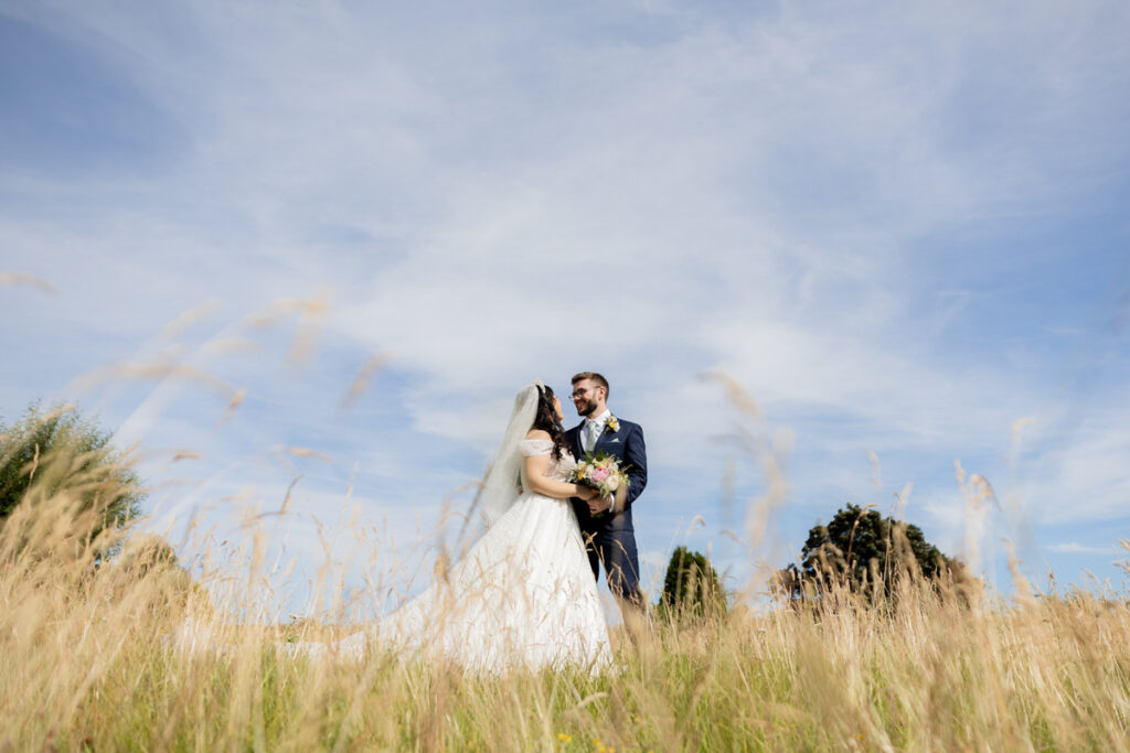 bride and groom standing in long grass during couple photo session in grounds of wootton park