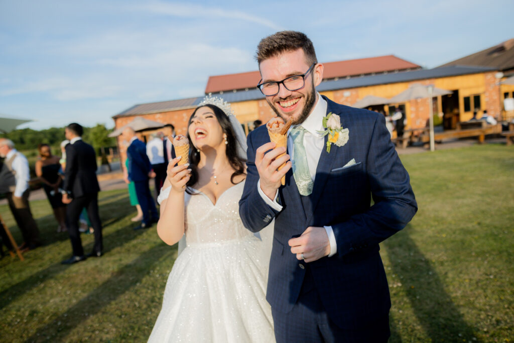 groom eating ice cream with bride laughing behind him during drinks reception at wootton park