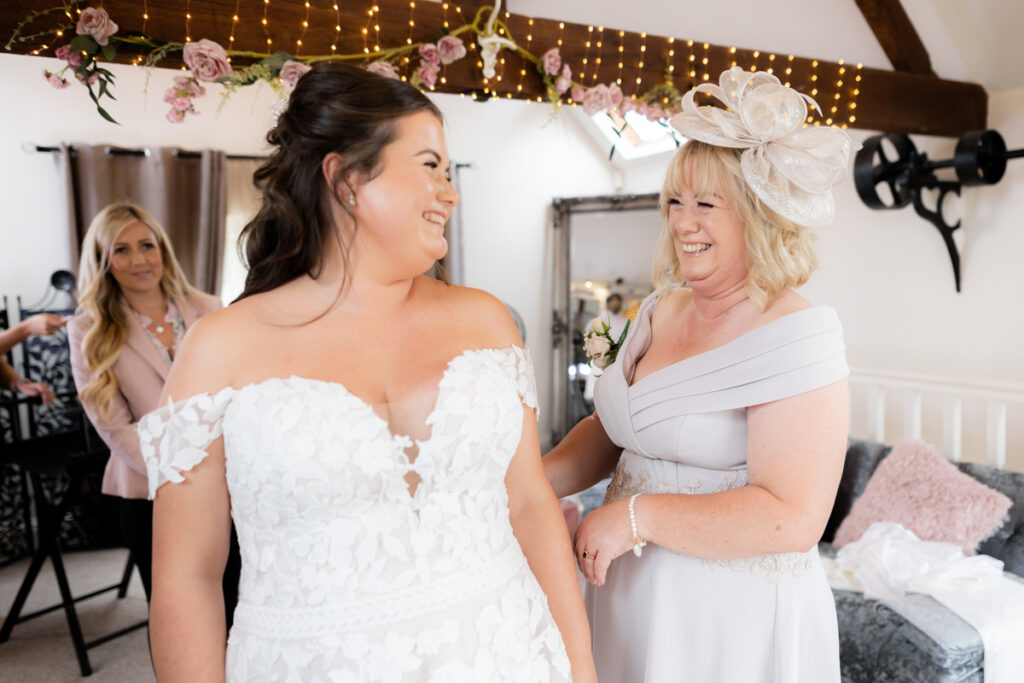 bride and mum laughing getting dressed for wedding day at bordesley park in tudor barn during bride prep