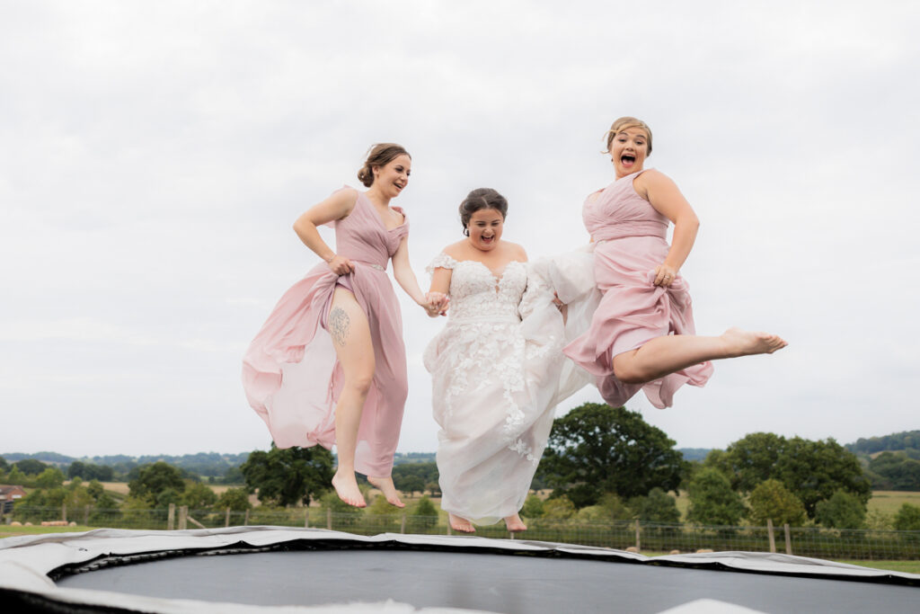 bride and two bridesmaids jumping on trampoline during drinks reception at bordesley park
