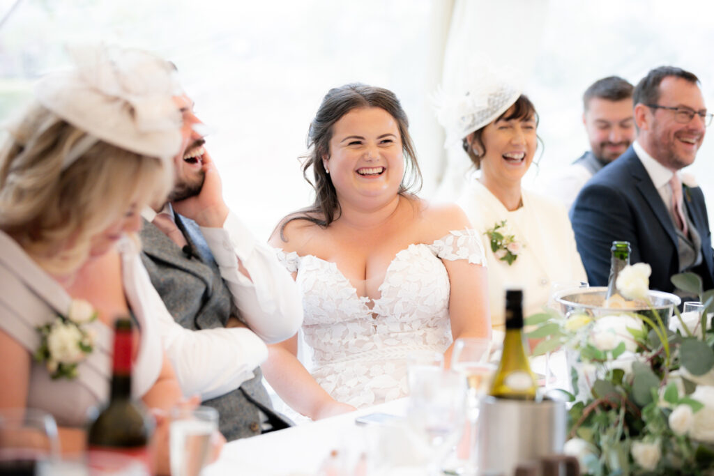 bride laughing during wedding breakfast in the marquee at bordesley park on summer wedding day