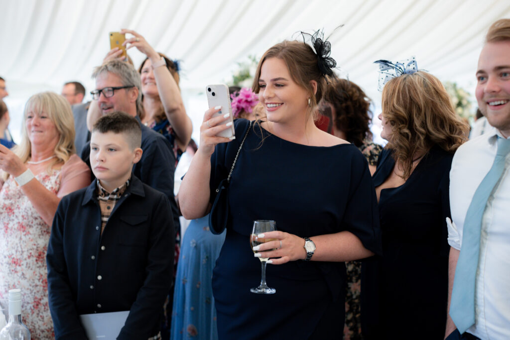 lady taking a photo during wedding breakfast in the marquee at bordesley park on summer wedding day