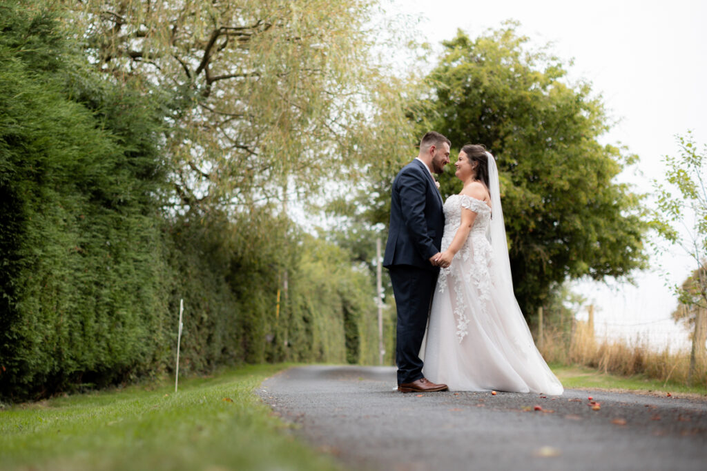 bride and groom standing togehter on driveway with trees in background during couple photos at bordesley park