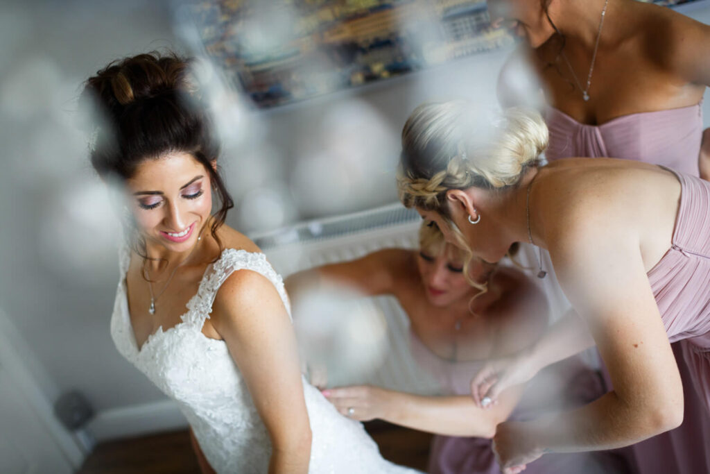 bride having her dress fastened by bridesmaids, taken from above by experienced wedding photographers still light photography