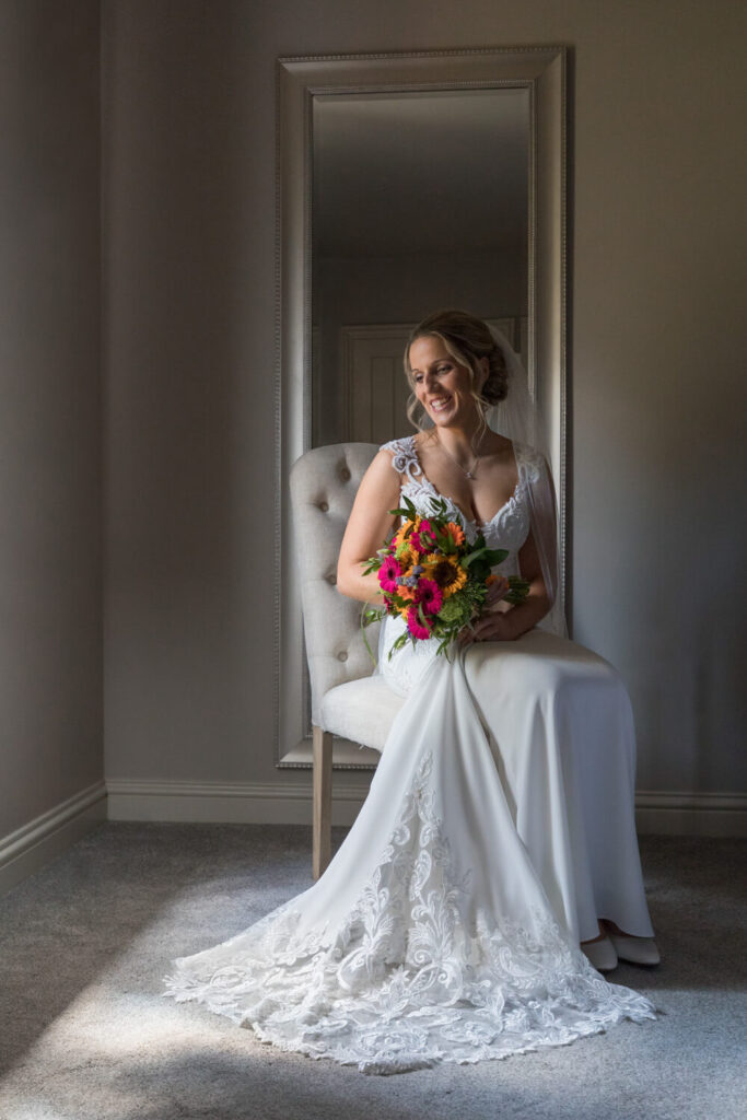 award winning wedding photograph of bride sitting in window light holding pink and orange flowers