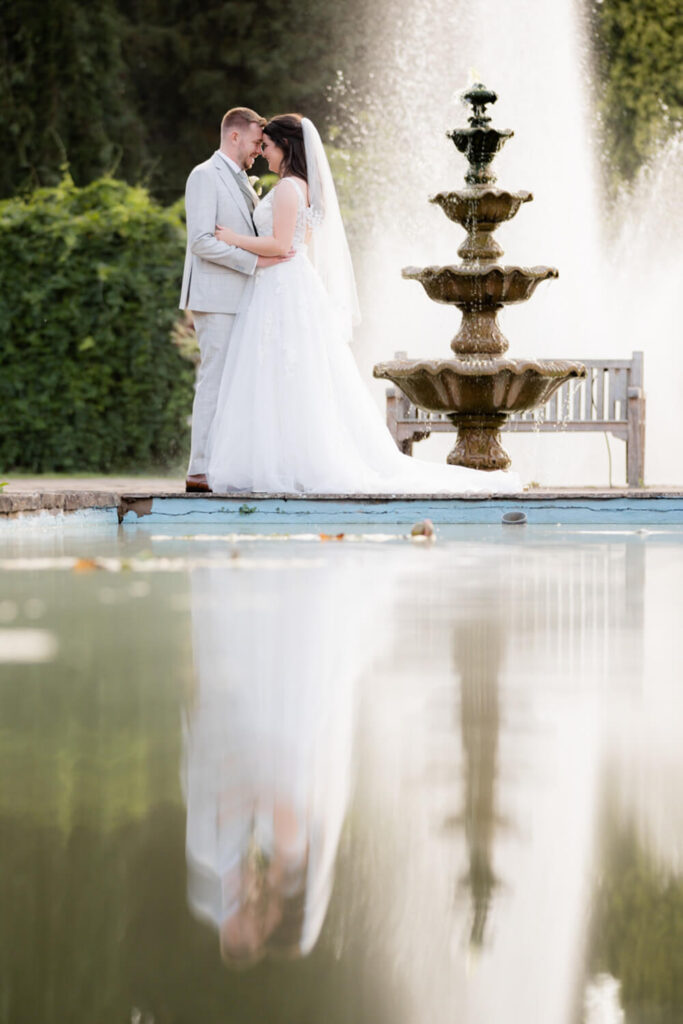 bride and groom embracing standing next to fountain at arley house and gardens, taken by experienced wedding photographers still light photography