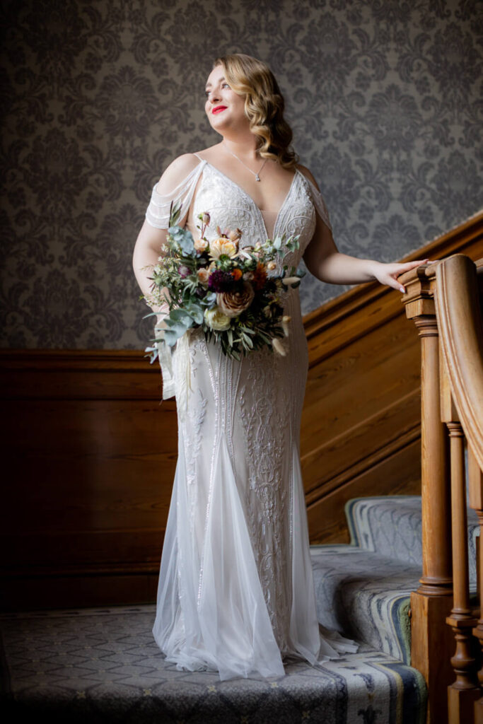bride wearing vintage dress standing on staircase at brockencote hall, by experienced wedding photographers still light photography