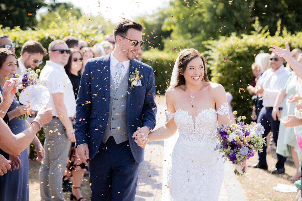 couple walking towards camera under confetti being thrown, taken by experienced wedding photographers still light photography
