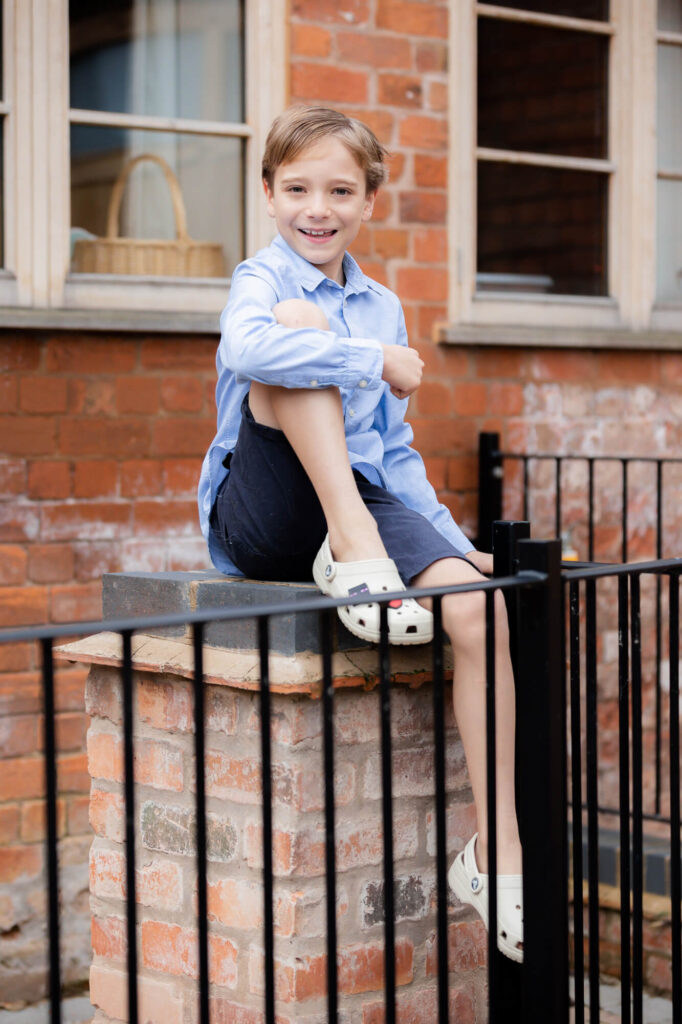 boy sat on brick ewall smiling at camera  during an outdoor family photography session in worcestershire