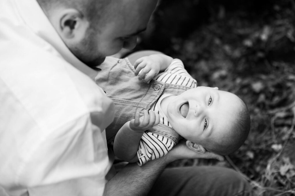 black and white image taken from above of laughing baby in dad's arms during an outdoor family photography session in worcestershire