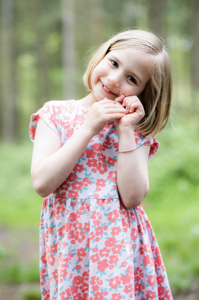 young girl wearing red flowery dress smiling at camera  during an outdoor family photography session in worcestershire