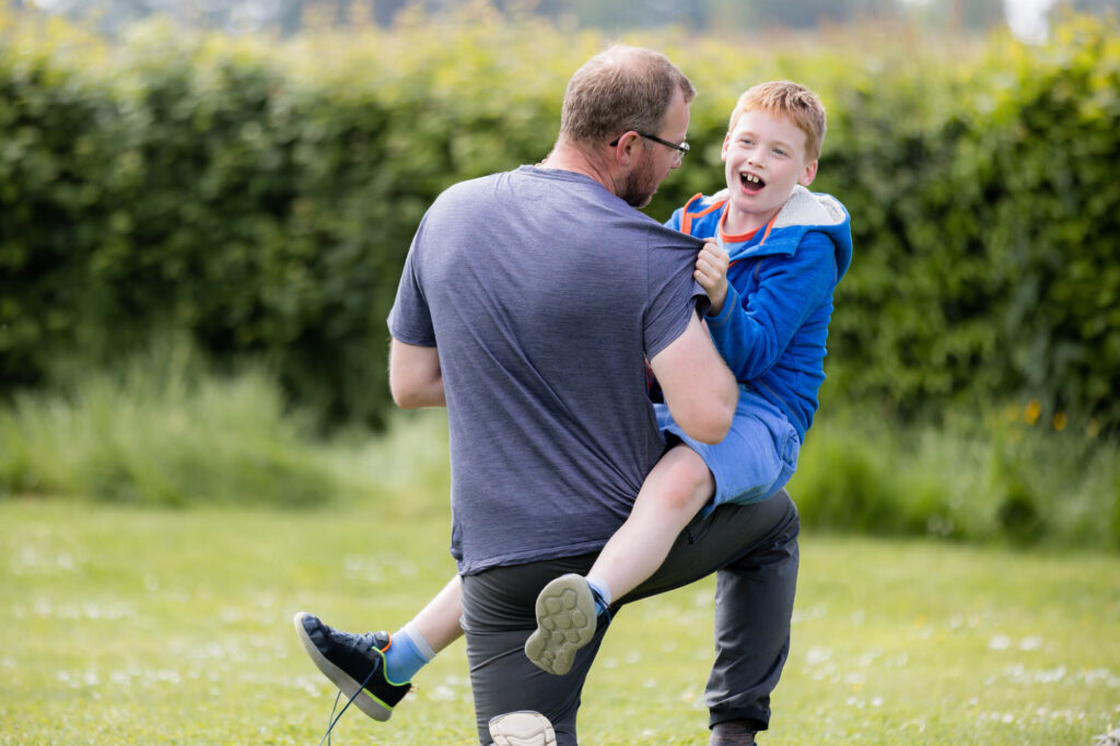 boy fun wrestling with dad during an outdoor family photography session in worcestershire