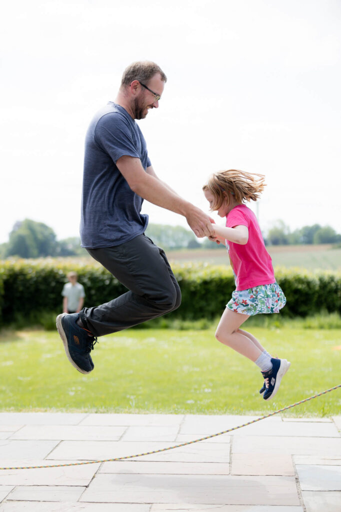 dad and daughter jumping skipping rope during an outdoor family photography session in worcestershire