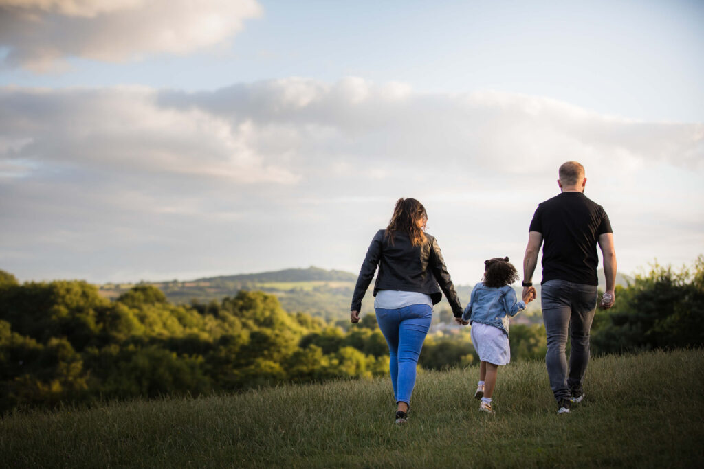 couple with their young daughter walking away from camera on hill top at dusk during an outdoor family photography session in worcestershire